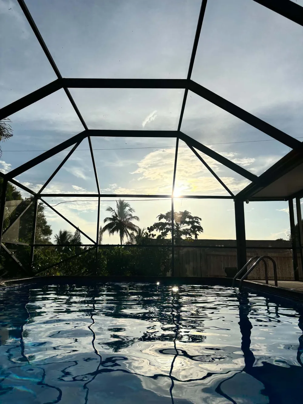 Heated screened-in pool at sunset, palm trees in silhouette